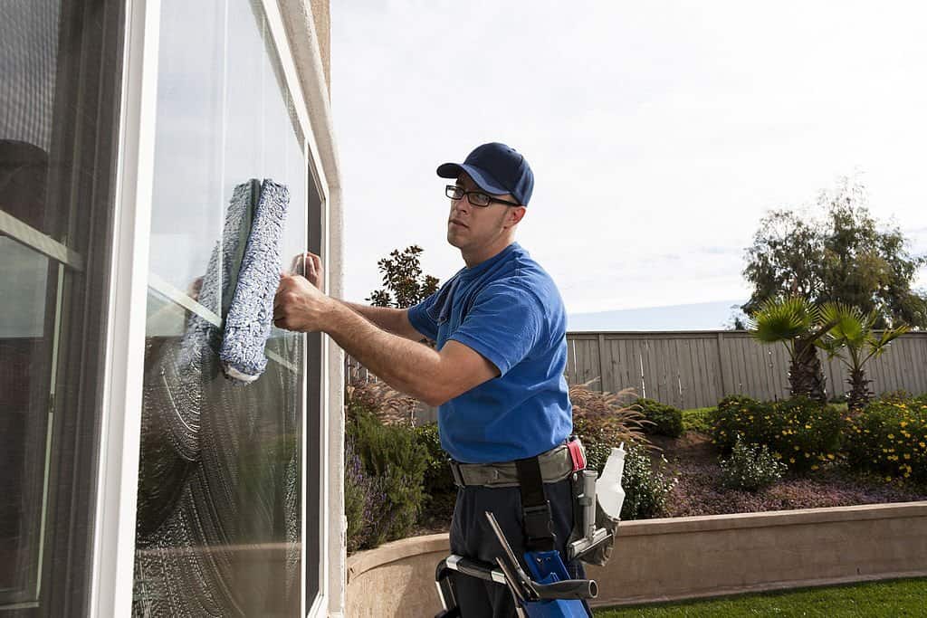 A worker cleaning a window using a squeegee, wearing a blue uniform and cap, from Triple Star Commercial Cleaning.