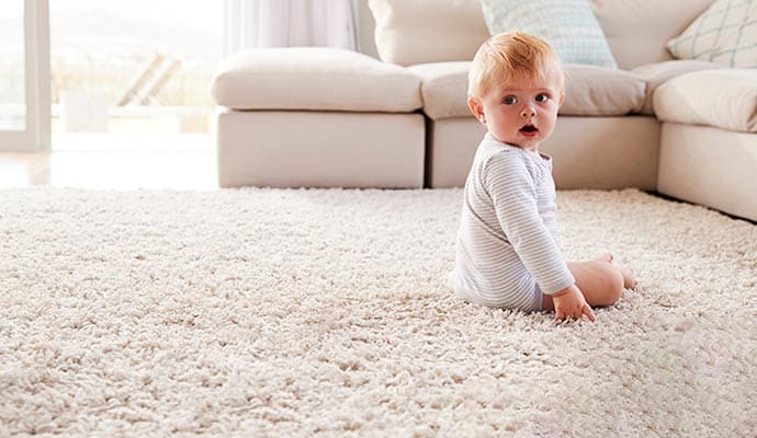 Baby sitting on a clean carpet in a cozy living room, emphasizing eco-friendly cleaning.