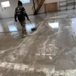 Professional cleaner using a pressure washing machine to clean a large concrete floor in an industrial space.