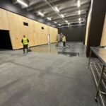 Two commercial cleaners using floor scrubber and vacuum on rubber flooring in Auckland venue