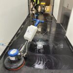 Commercial cleaner using rotary scrubber on black vinyl floor in Auckland building