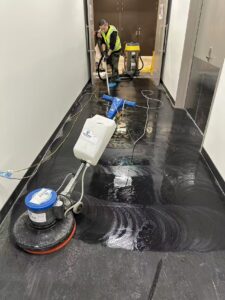 Commercial cleaner using rotary scrubber on black vinyl floor in Auckland building