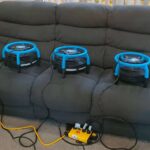 Three drying fans placed on a freshly cleaned dark recliner sofa