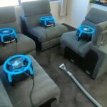 Lounge room with multiple grey couches and drying fans after cleaning